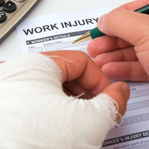 Person with bandaged hand filling out Work Injury Claim form - LAW OFFICES OF JEFFREY M. BLOOM