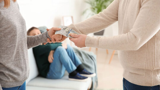 Couple exchanging money, with a child in the background, representing spousal support.