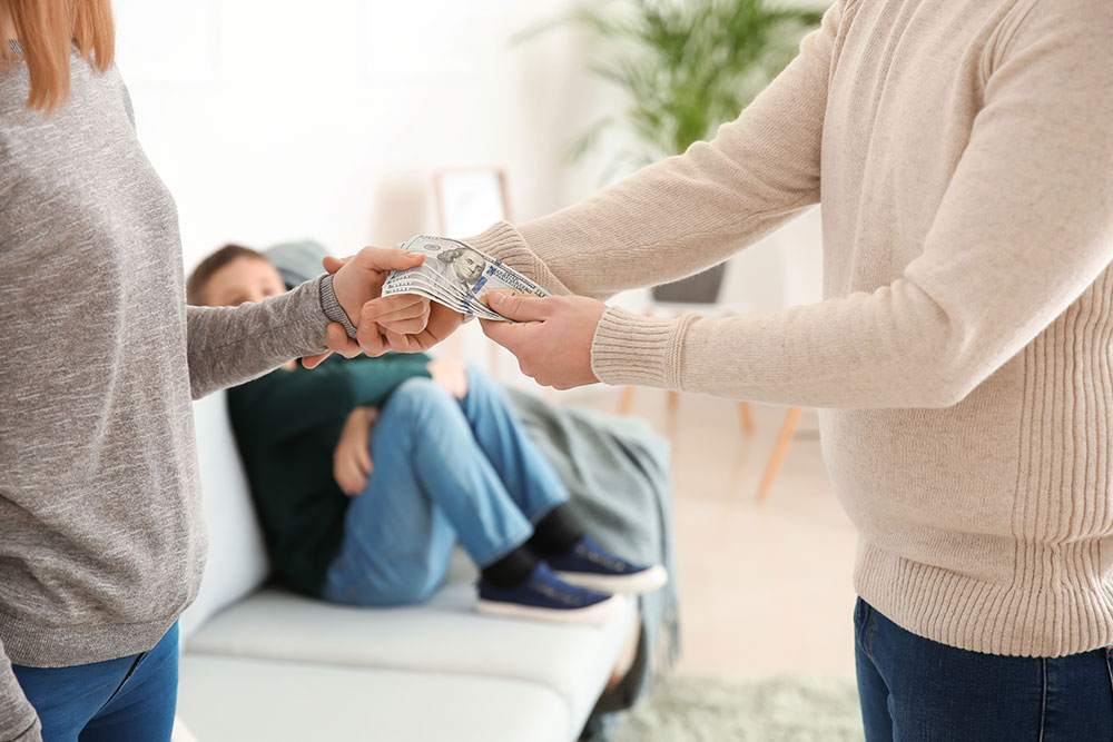 Couple exchanging money, with a child in the background, representing spousal support.